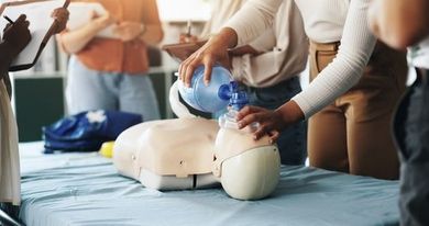 People practicing CPR on a training manikin, with one person using a bag valve mask.