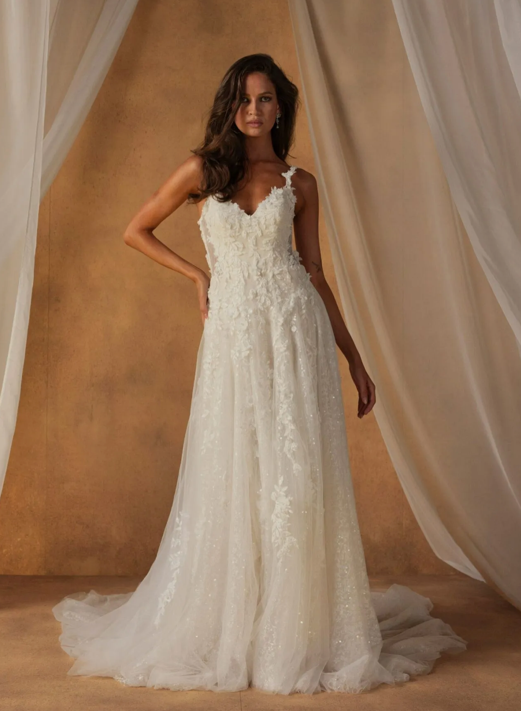 Nita  van Madi Lane heeft een trompet silhouet met een laag glitter tule om een ​​extra glans toe te voegen aan haar all-over pailletten kantpatroon. Haar lijfje is ontworpen met een moderne, trendy piek-stijl halslijn met een sexy maar ingetogen illusie plunge. 