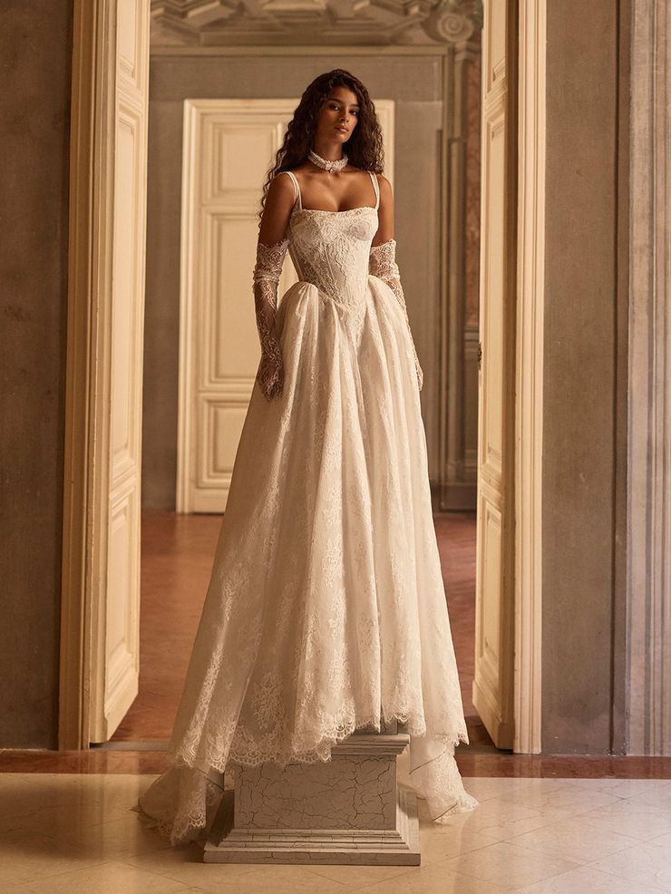 Chantilly lace A-line gown featuring a cupless corset bodice with a square neckline and delicate straps. The full, sweeping skirt is finished with chantilly lace-covered decorative buttons, creating a refined and timeless silhouette.
Pairs beautifully with the Arlisse or Iverly choker and Odyssia gloves, landing the look on its final, romantic 