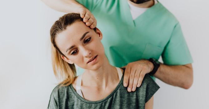 Physical therapist gently stretching a woman's neck and shoulder in a clinic setting
