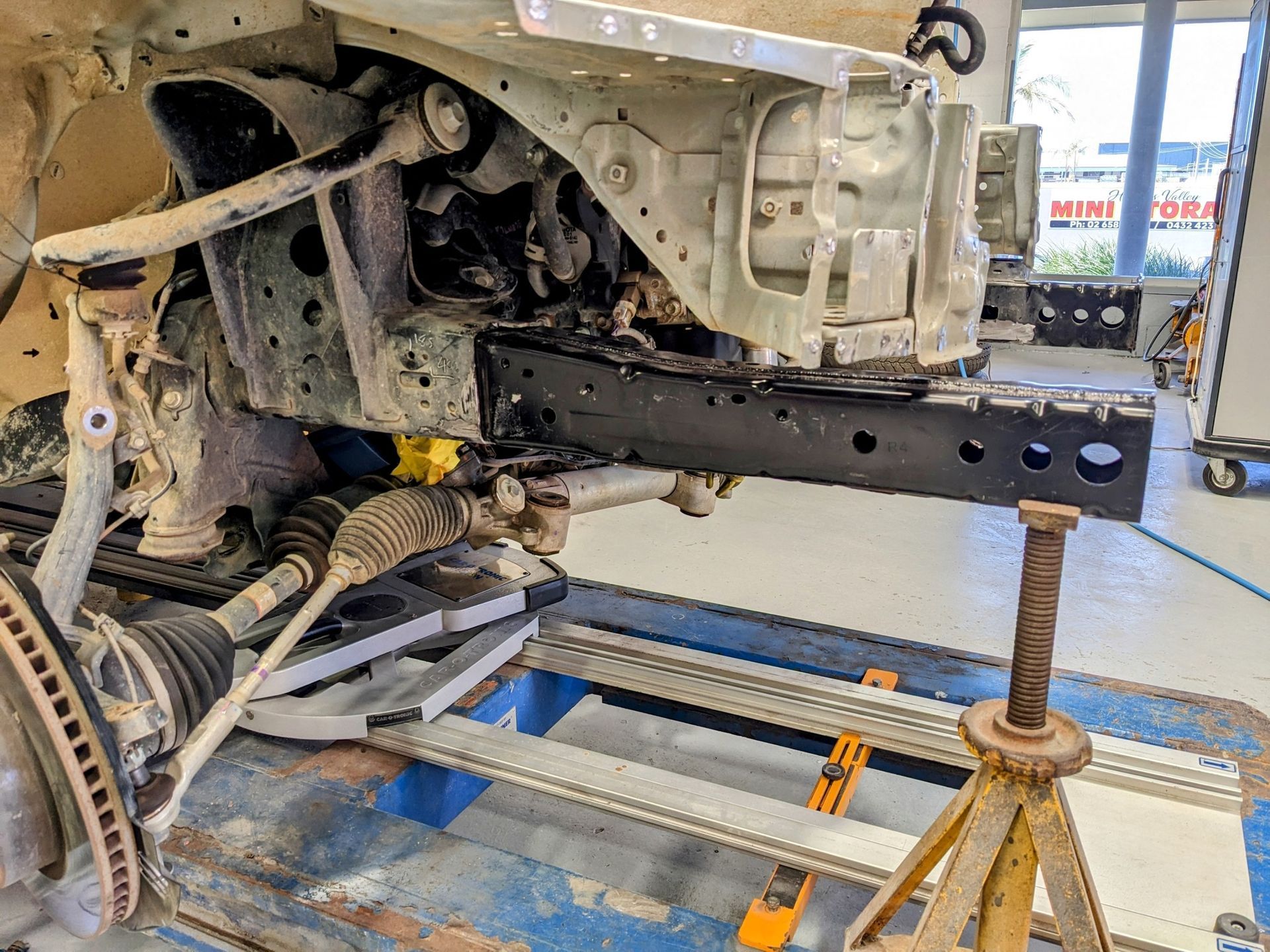 Car Frame Front End Repair, Black Metal Support Beam, on a Lift in a Shop — Supalook Smash Repairs In Port Macquarie, NSW