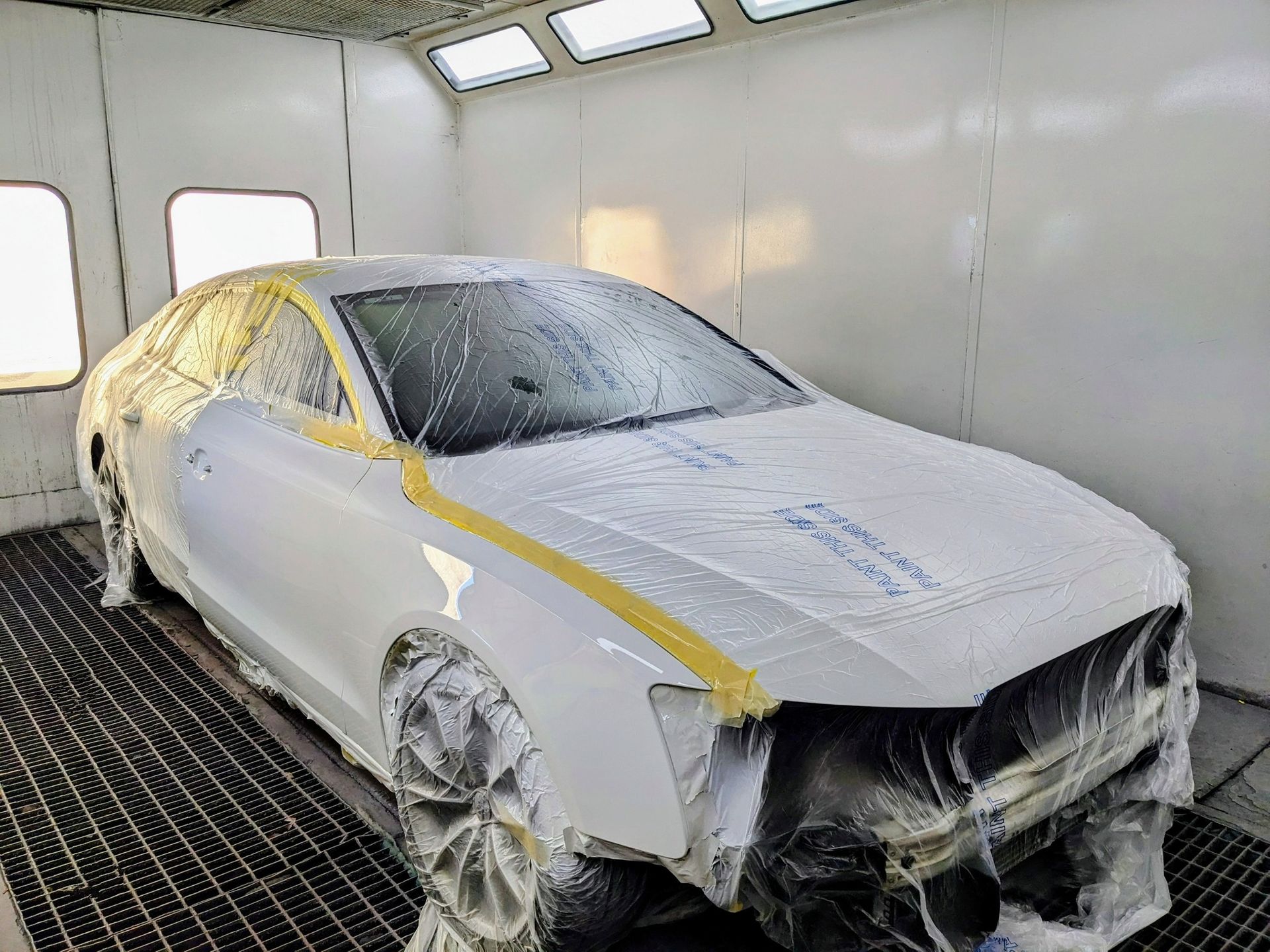 A white car masked with protective plastic and tape, prepared for painting inside a spray booth  — Supalook Smash Repairs In Port Macquarie, NSW