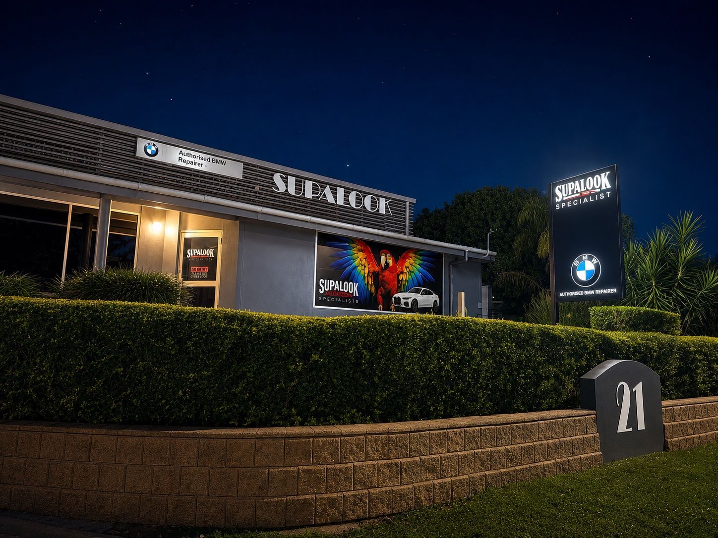 Night view of a lit retail building with a digital  — Supalook Smash Repairs In Port Macquarie, NSW, hedge, and number 21 address marker.