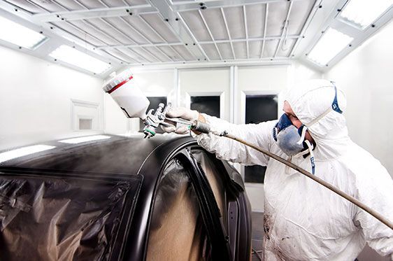 Person in Protective Suit Spray-painting a Black Car in a Paint Booth — Supalook Smash Repairs In Port Macquarie, NSW