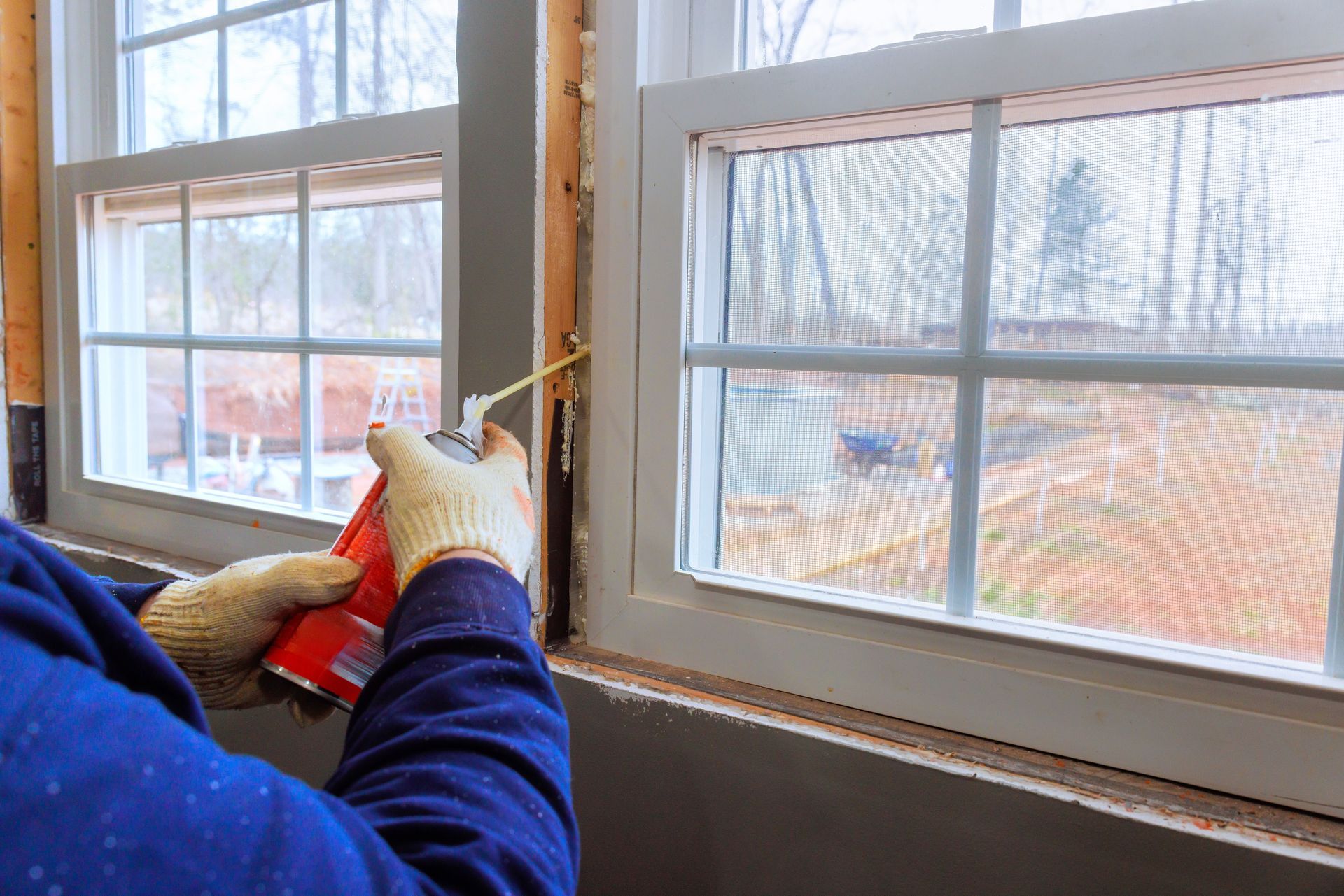 Person cleaning a window with red cloth while wearing gloves, sunlight visible through the glass.