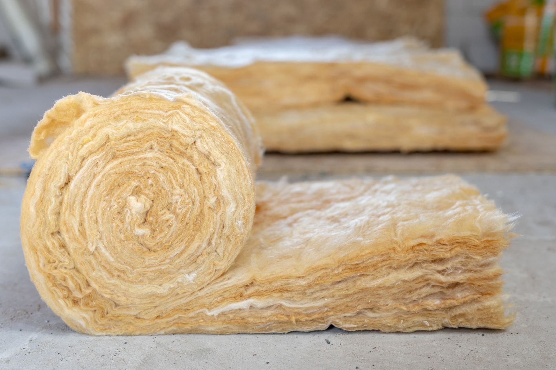 Rolled beige wool insulation batts stacked on a gray surface