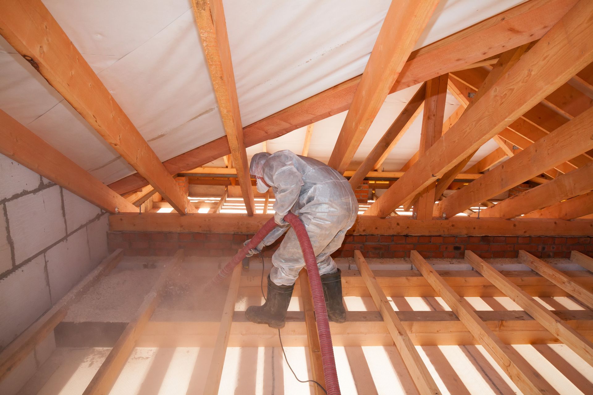 Worker spraying insulation in an attic with exposed wooden rafters