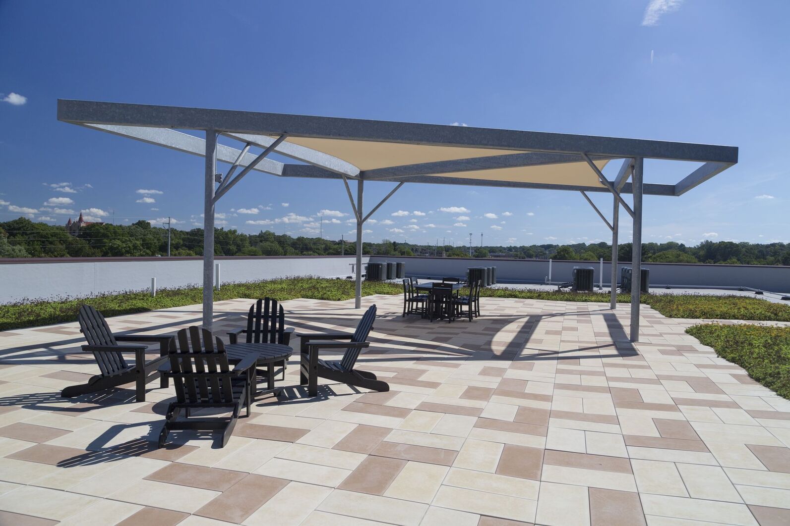 Shaded picnic area with tables and benches on a paved lakeside patio under a blue sky