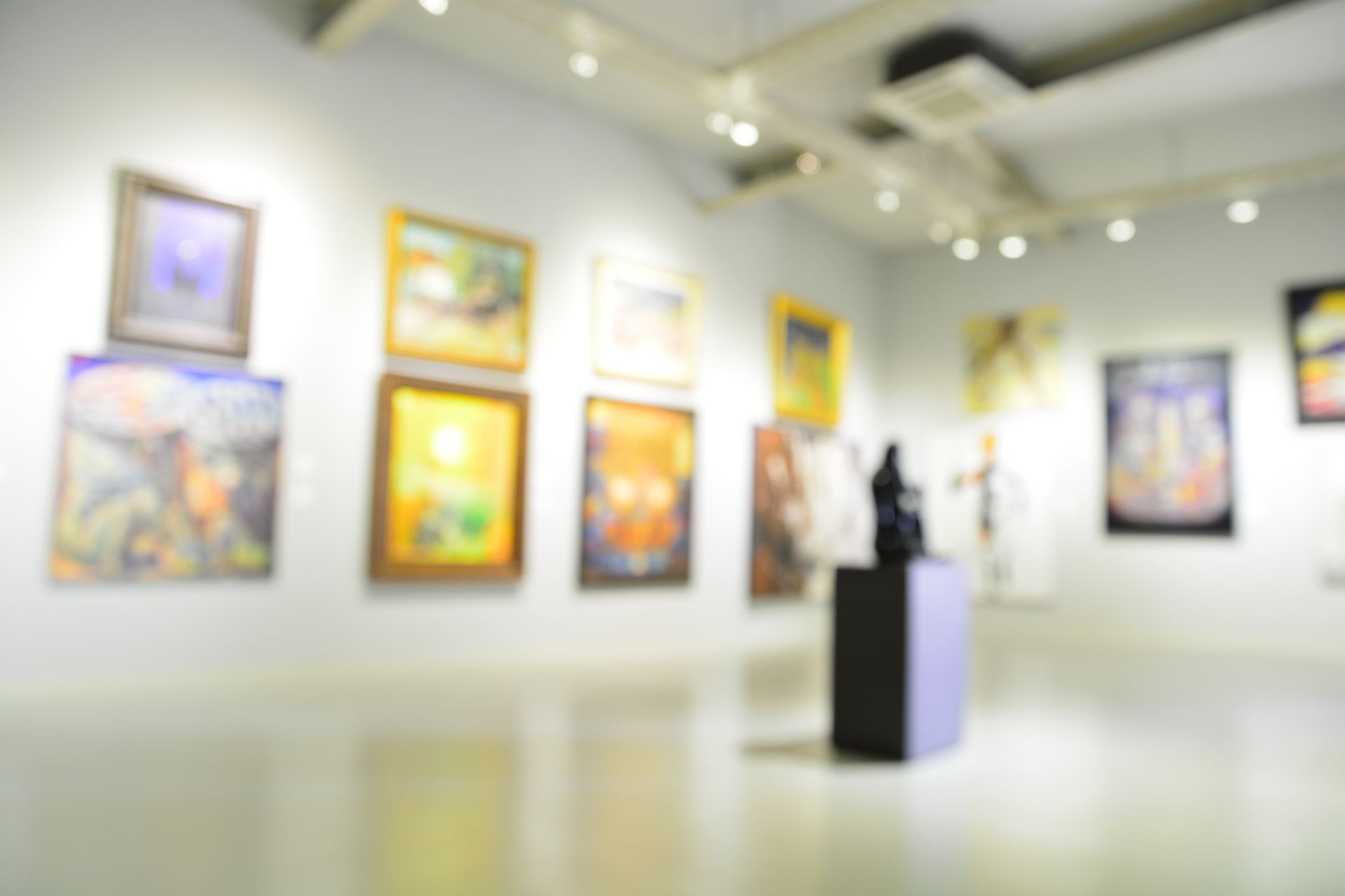 Blurred art gallery with colorful framed paintings and a sculpture on a pedestal under spotlights