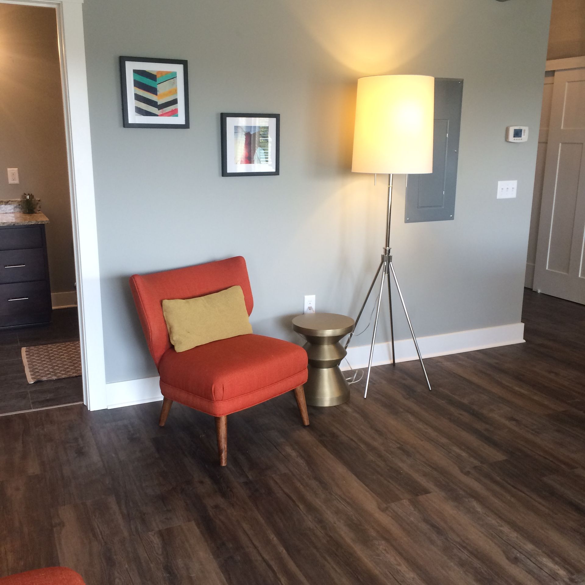 Cozy living room corner with orange chair, floor lamp, small table, wall art, and dark wood flooring