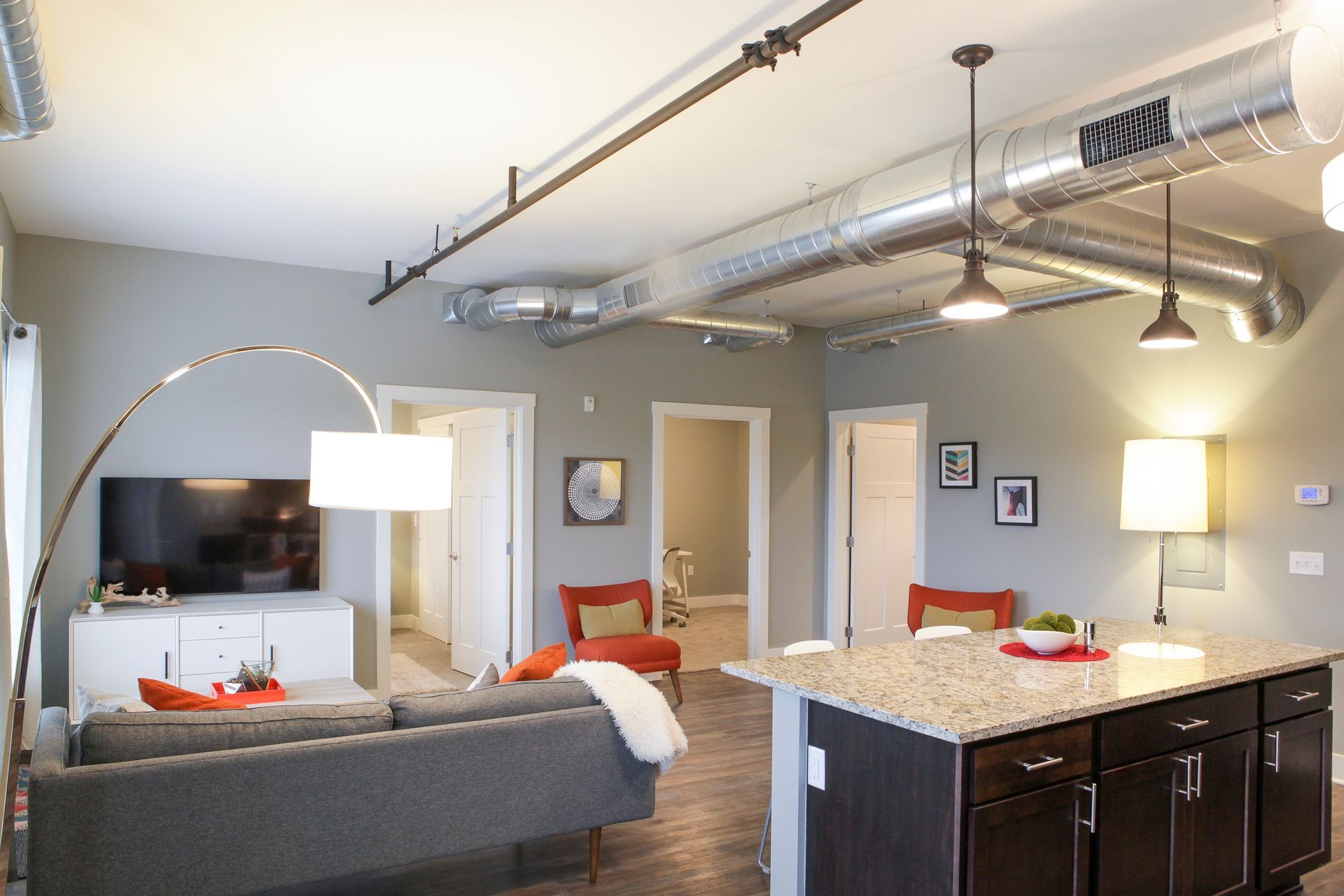 Modern open-plan living room with gray sofa, TV, floor lamp, and kitchen island under exposed ductwork
