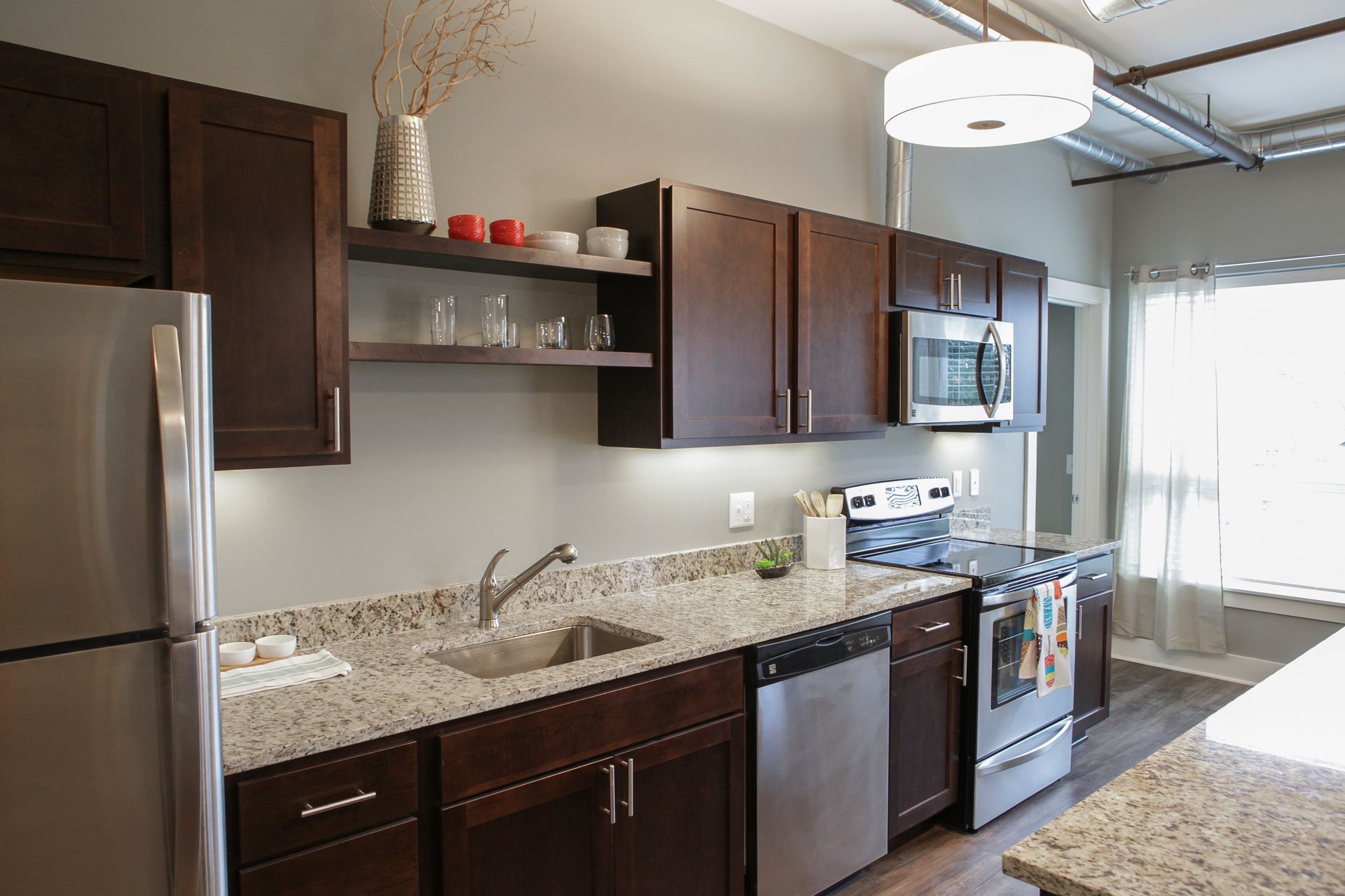 Modern kitchen with dark wood cabinets, granite counters, stainless appliances, and a window by the dining area