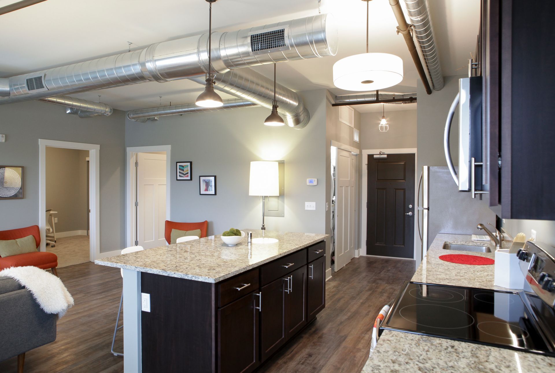 Modern open-plan kitchen and living area with granite island, dark cabinets, exposed ductwork, and wood floors