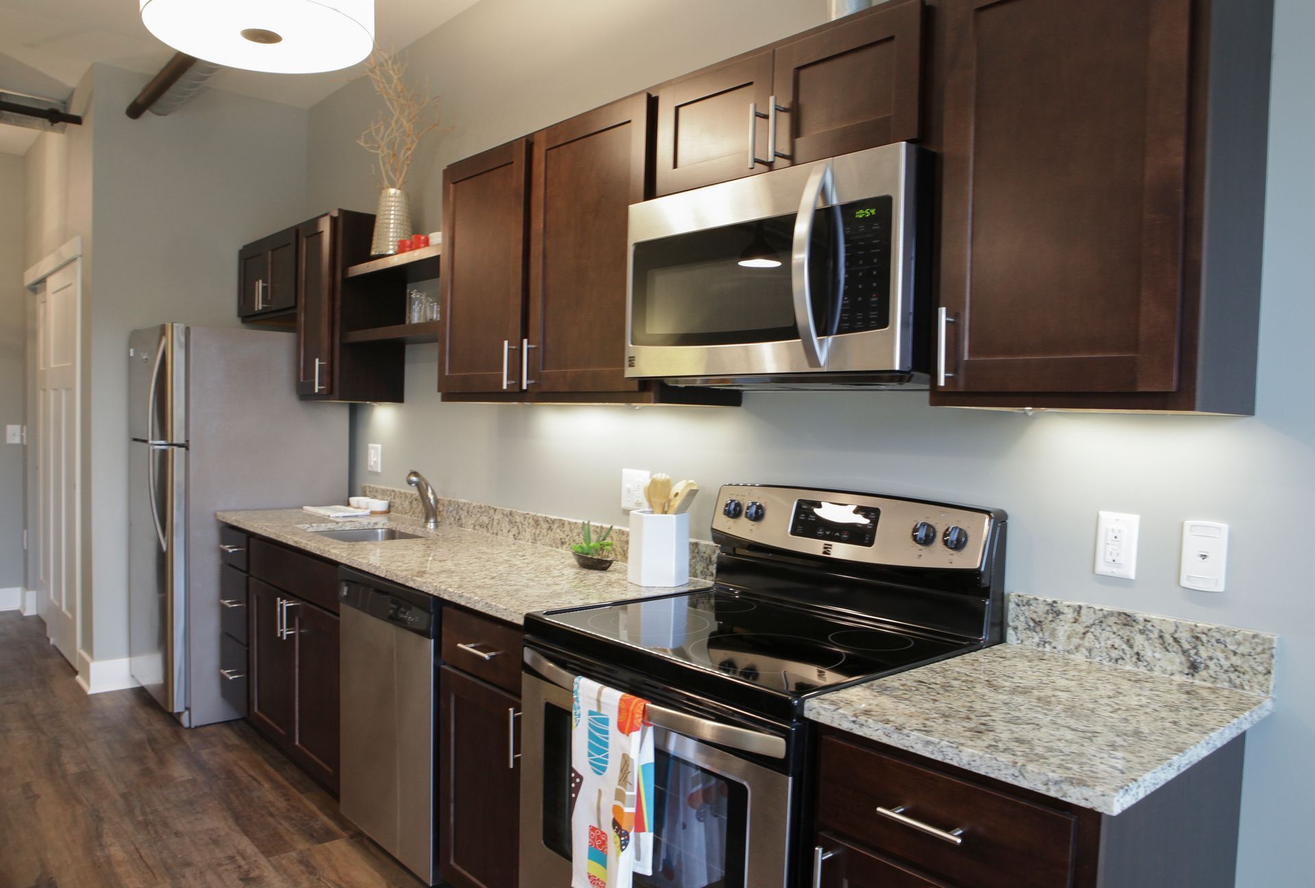 Modern kitchen with dark cabinets, granite counters, stainless steel appliances, and hardwood floors
