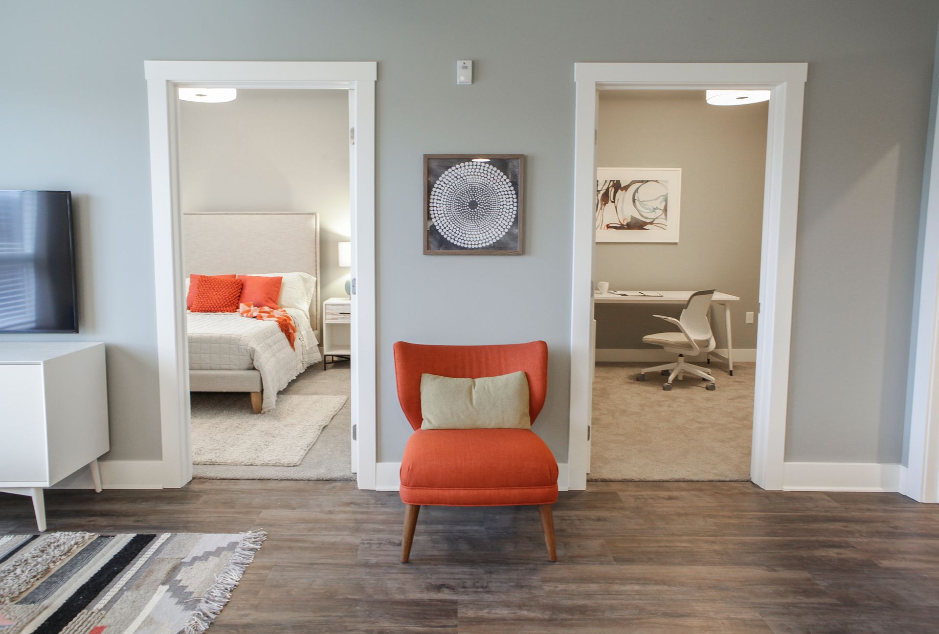 Modern room with three doorways, orange chair, and visible bedroom and office spaces