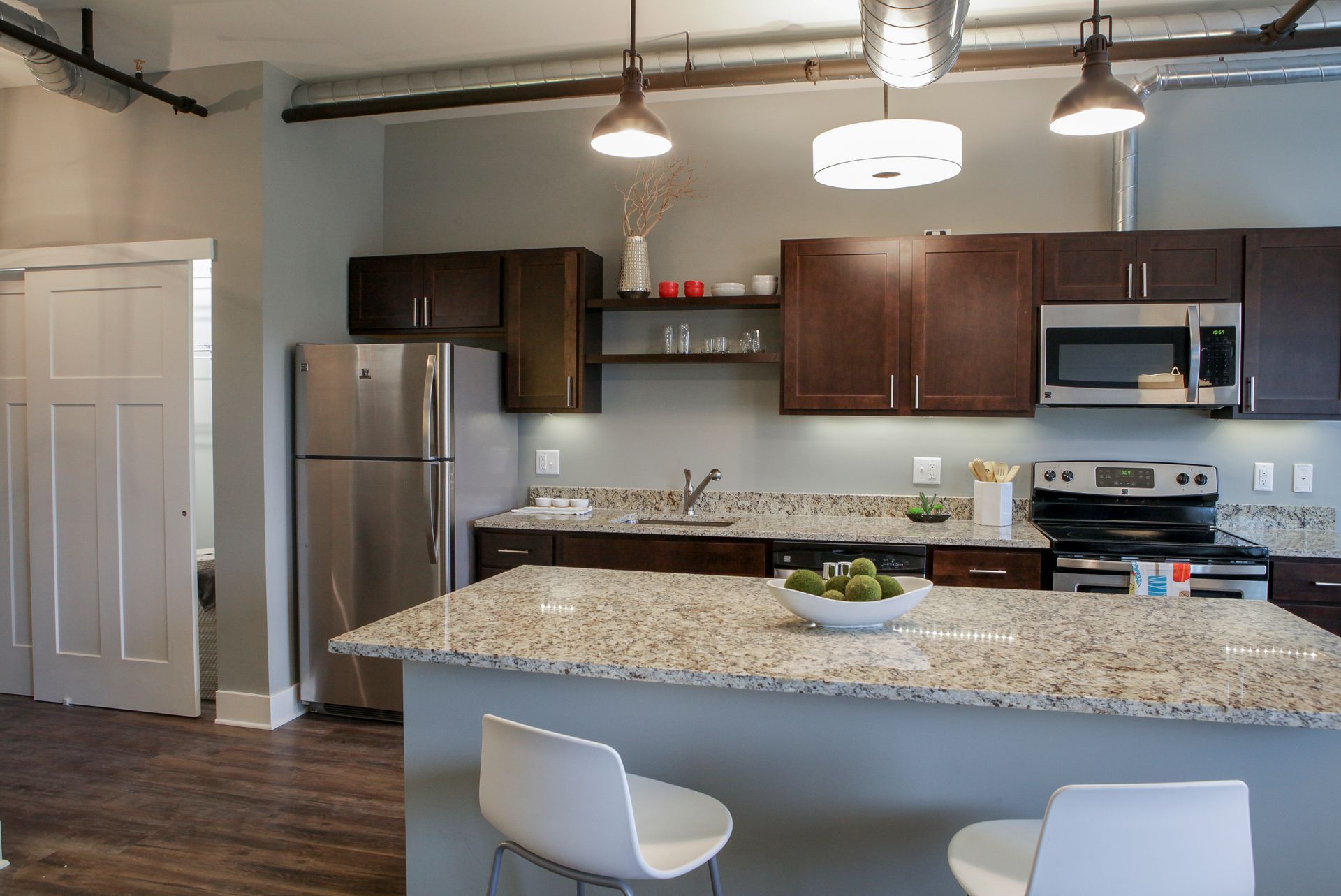 Modern kitchen with granite island, dark cabinets, stainless appliances, and two white barstools