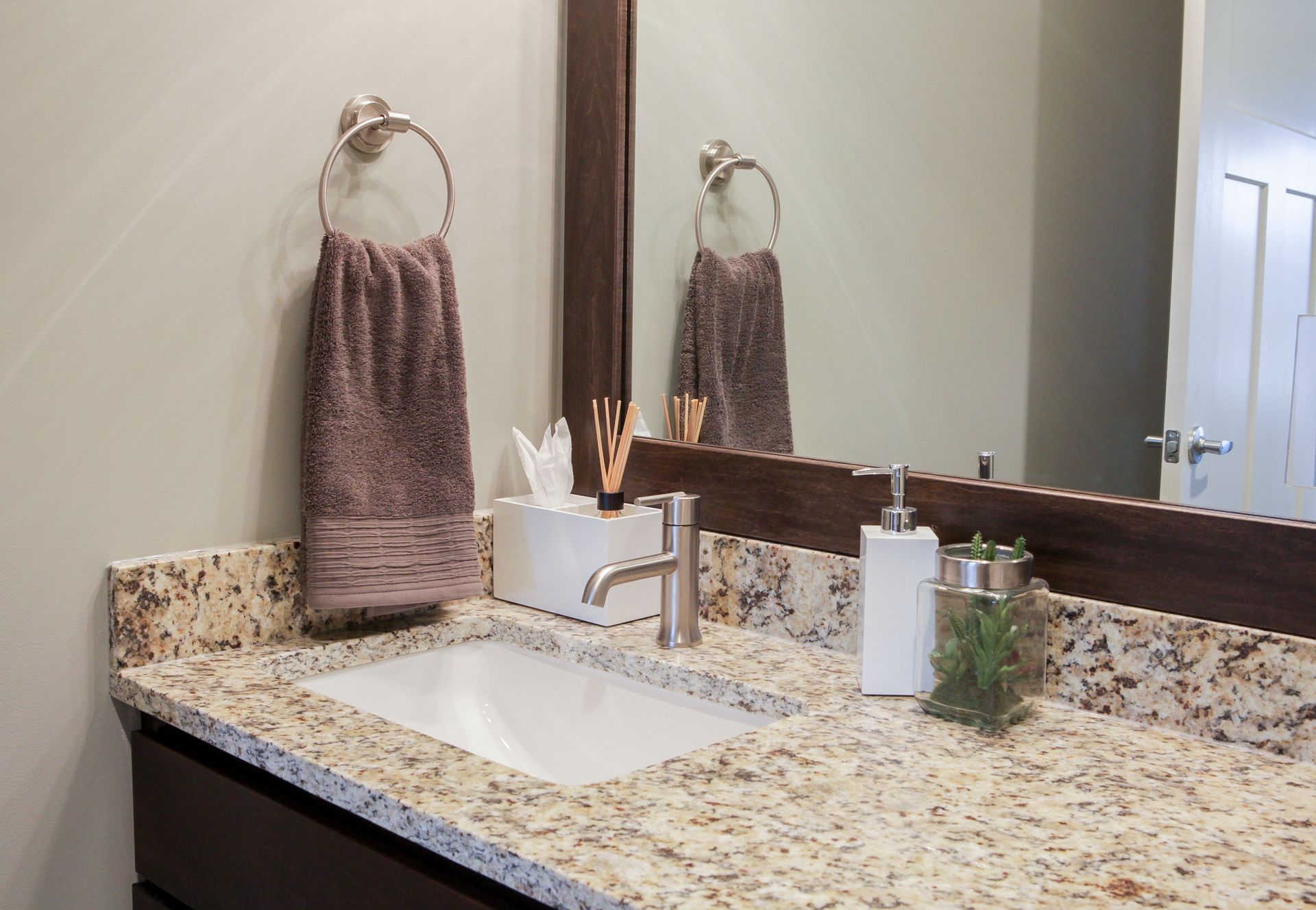Bathroom vanity with granite countertop, sink, faucet, towels, soap dispenser, and mirror