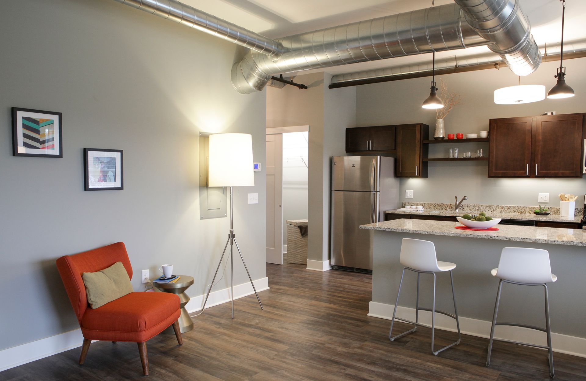 Modern open-plan apartment with kitchen, bar stools, orange chair, and floor lamp