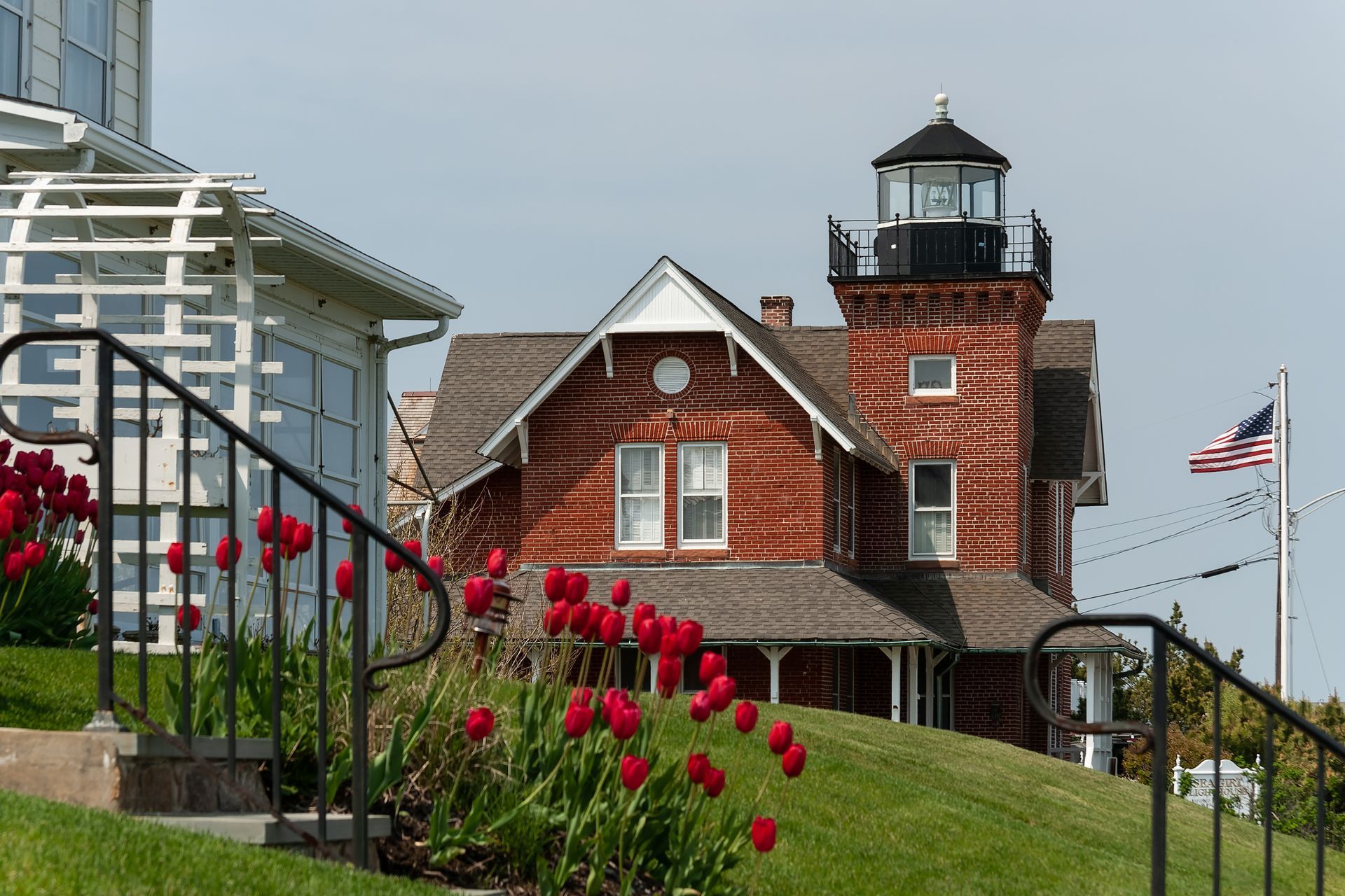 A lighthouse is sitting on top of a hill next to a house.
