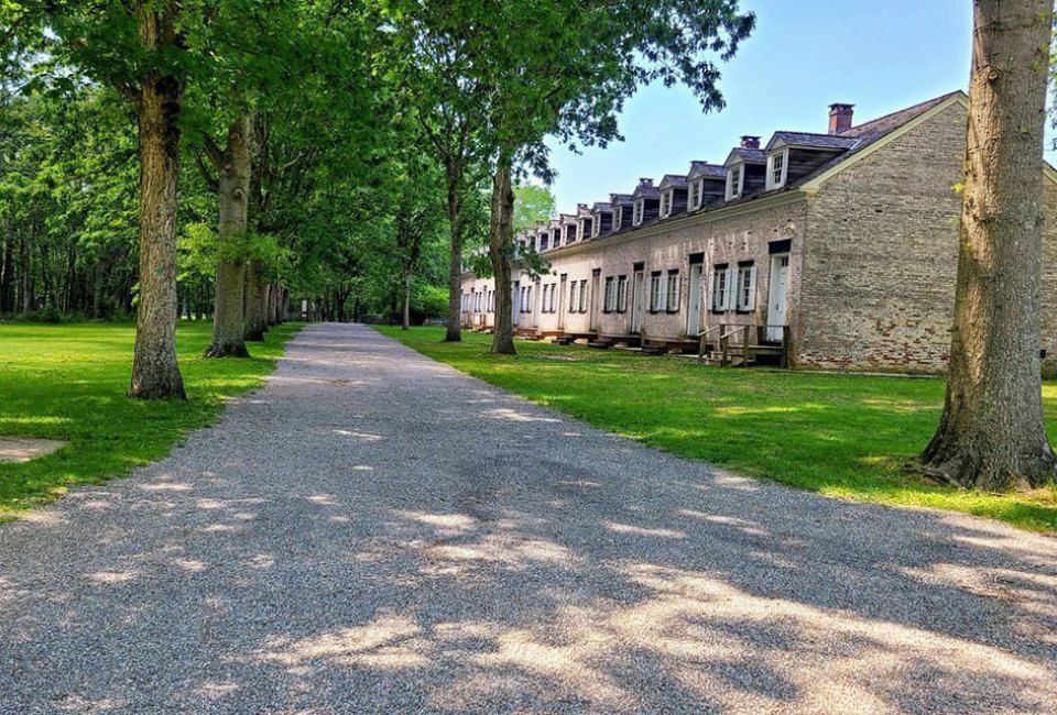 A gravel road leading to a row of buildings surrounded by trees.