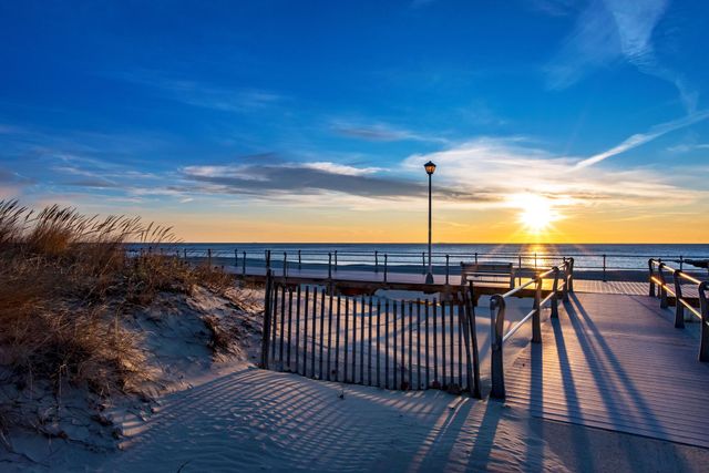 The sun is setting over the ocean behind a fence on the beach.