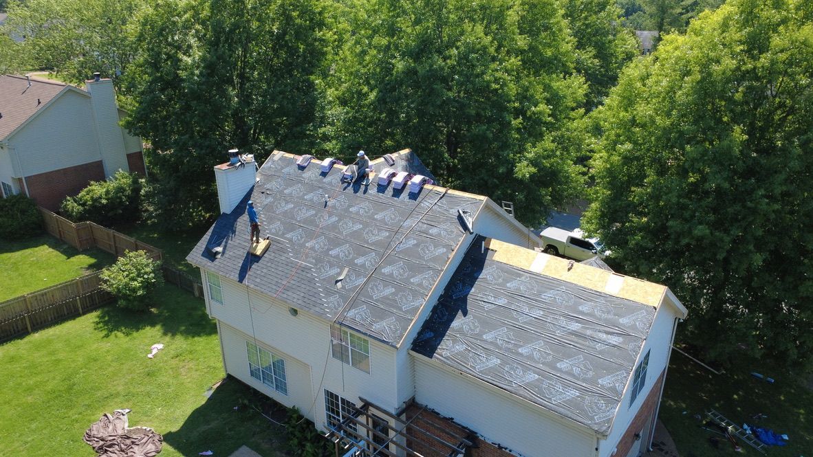 Roofers working on a white house roof surrounded by green trees on a sunny day