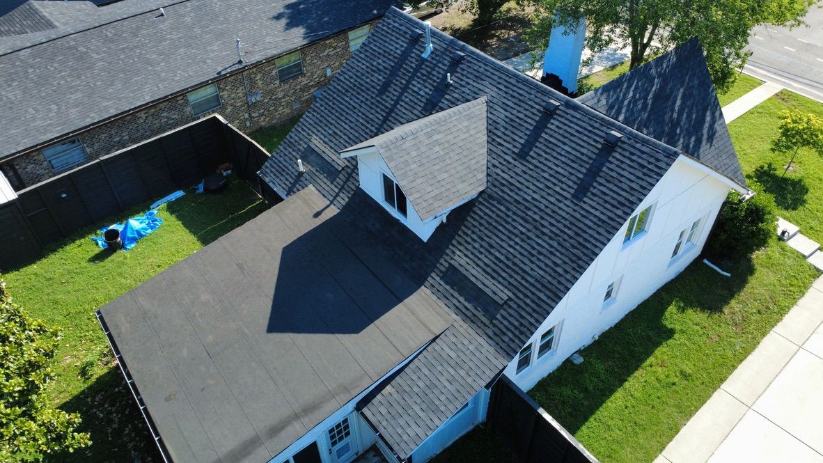 Aerial view of a house with dark gray roof, small dormer, and a fenced backyard with a blue pool.