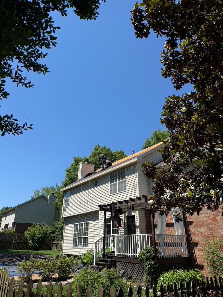 House with striped awning and porch framed by trees under a clear blue sky
