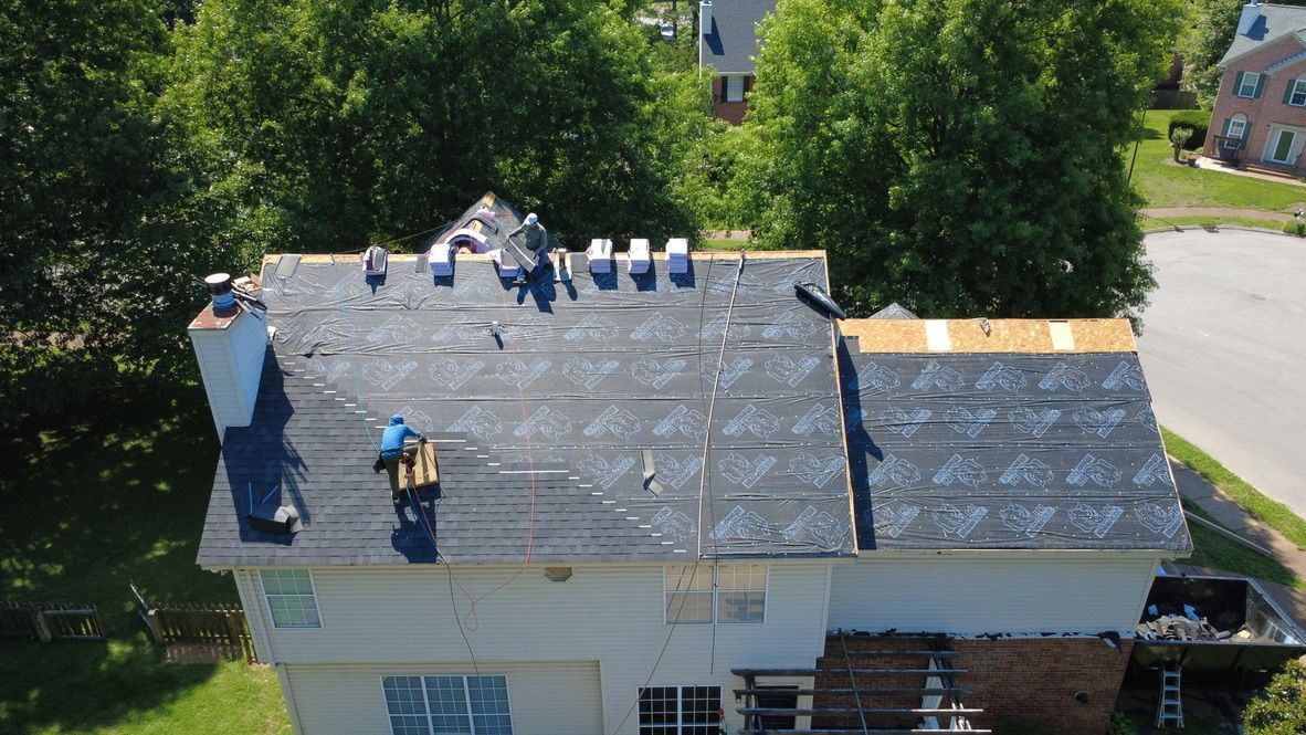 Roofers working on a house roof with gray shingles and roof materials nearby