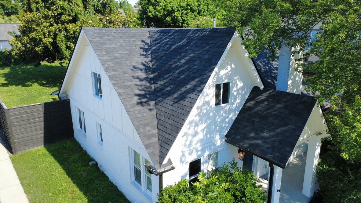 White house with dark gray roof surrounded by green trees and lawn, viewed from above