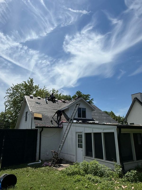 Backyard with a weathered house, black fence, sliding glass doors, and a bright blue sky with wispy clouds