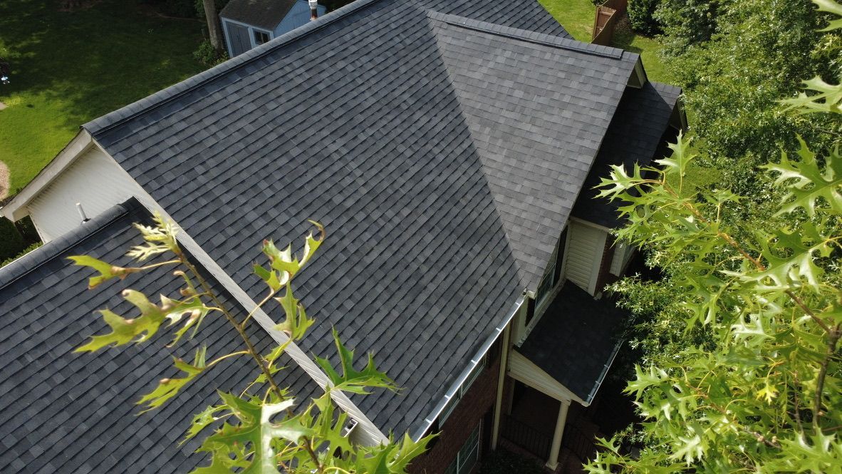 Aerial view of a house with a dark gray roof, partially framed by green trees.