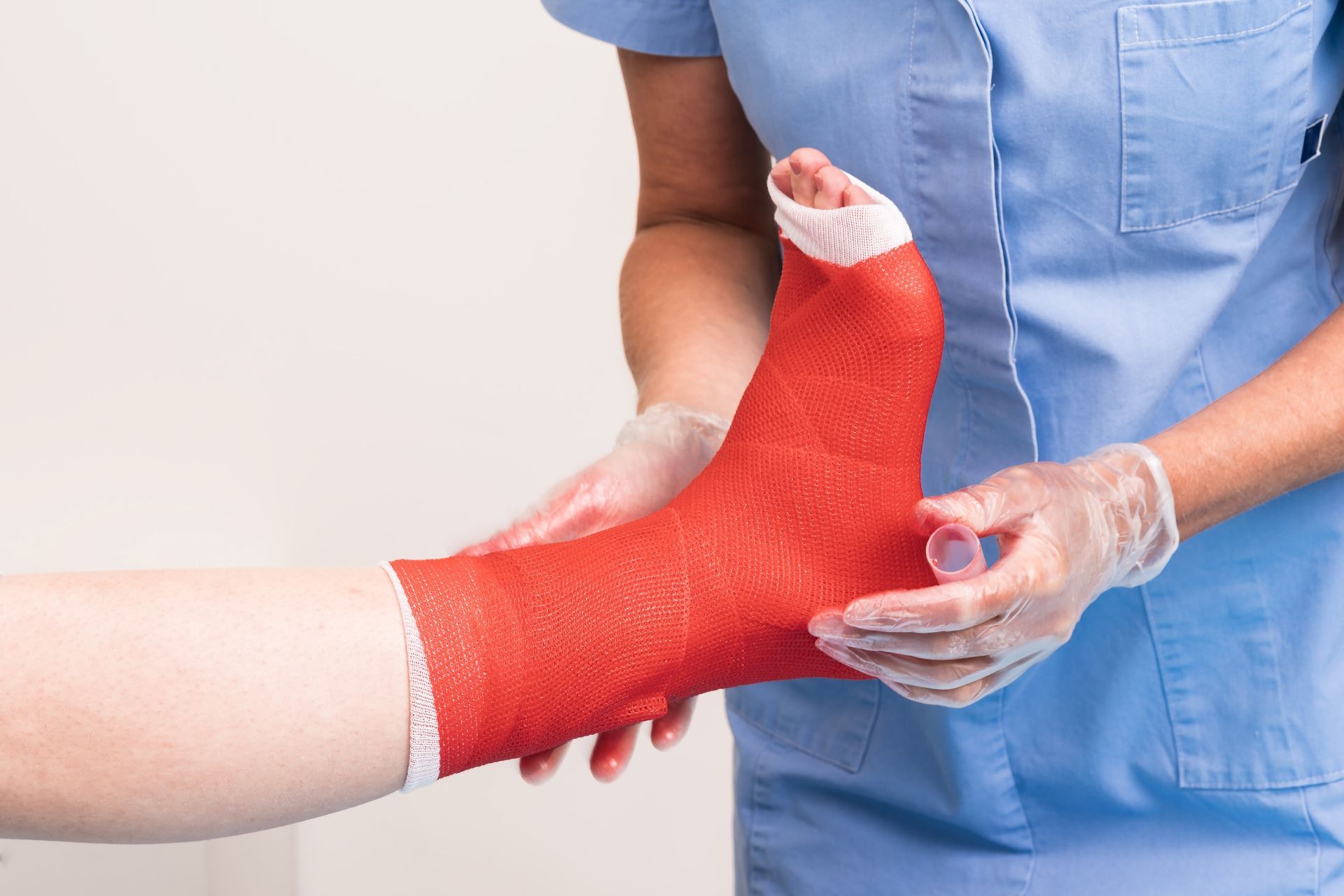 Person's foot in red cast, being held by a healthcare worker in a blue uniform and gloves.