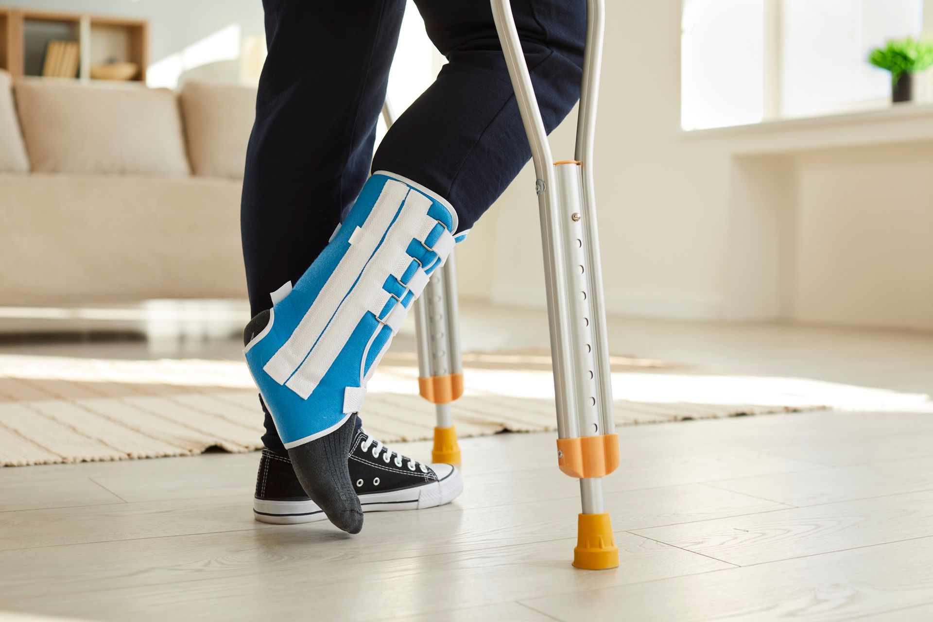 Person with leg brace using crutches indoors; leg is supported by a blue and white brace.