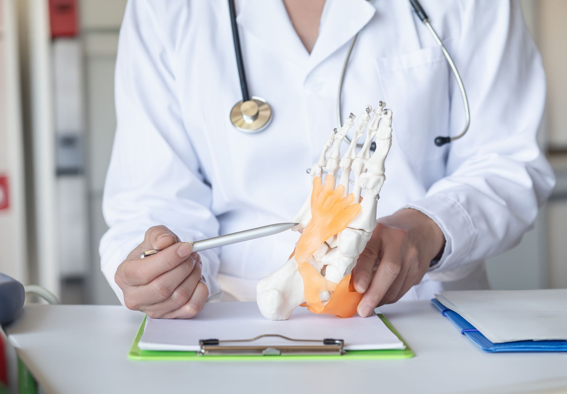 Doctor pointing to foot model, explaining anatomy, wearing white coat, stethoscope around neck.