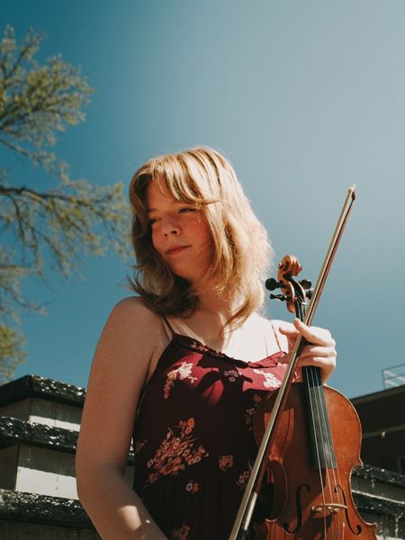 Headshot of Audrey Cox holding her violin and looking off into the distance.