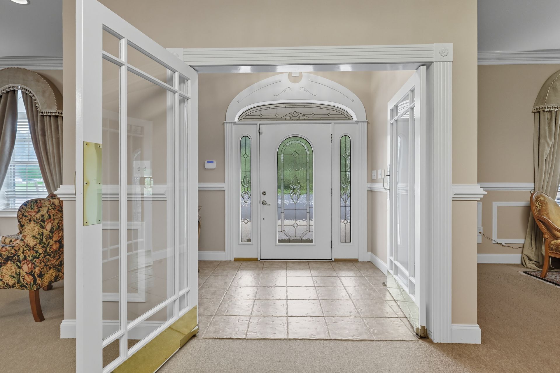 Elegant foyer with double glass doors, arched entryway, and tiled floor leading to a bright front entrance