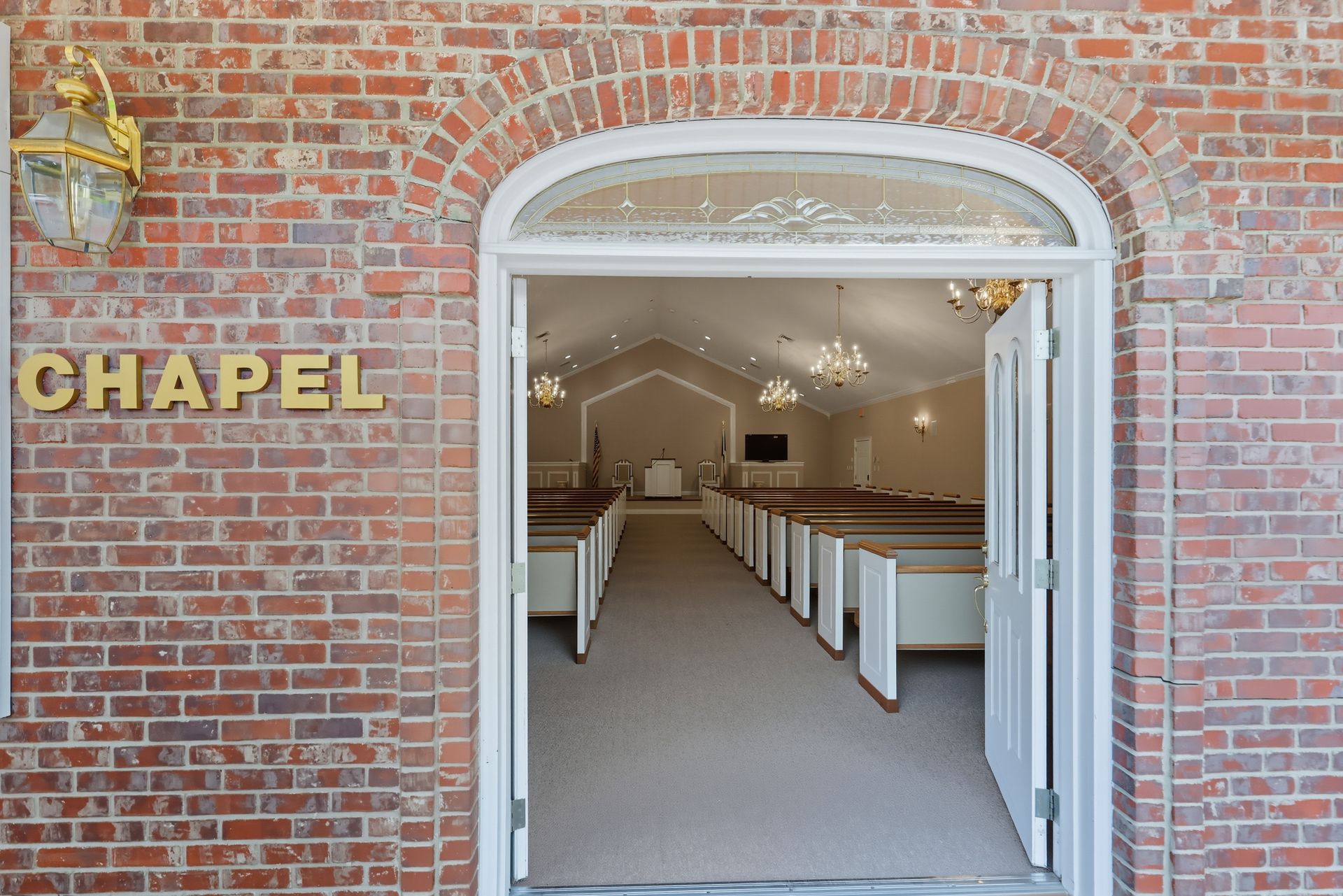 Open chapel doorway in a brick building, with white pews visible inside.