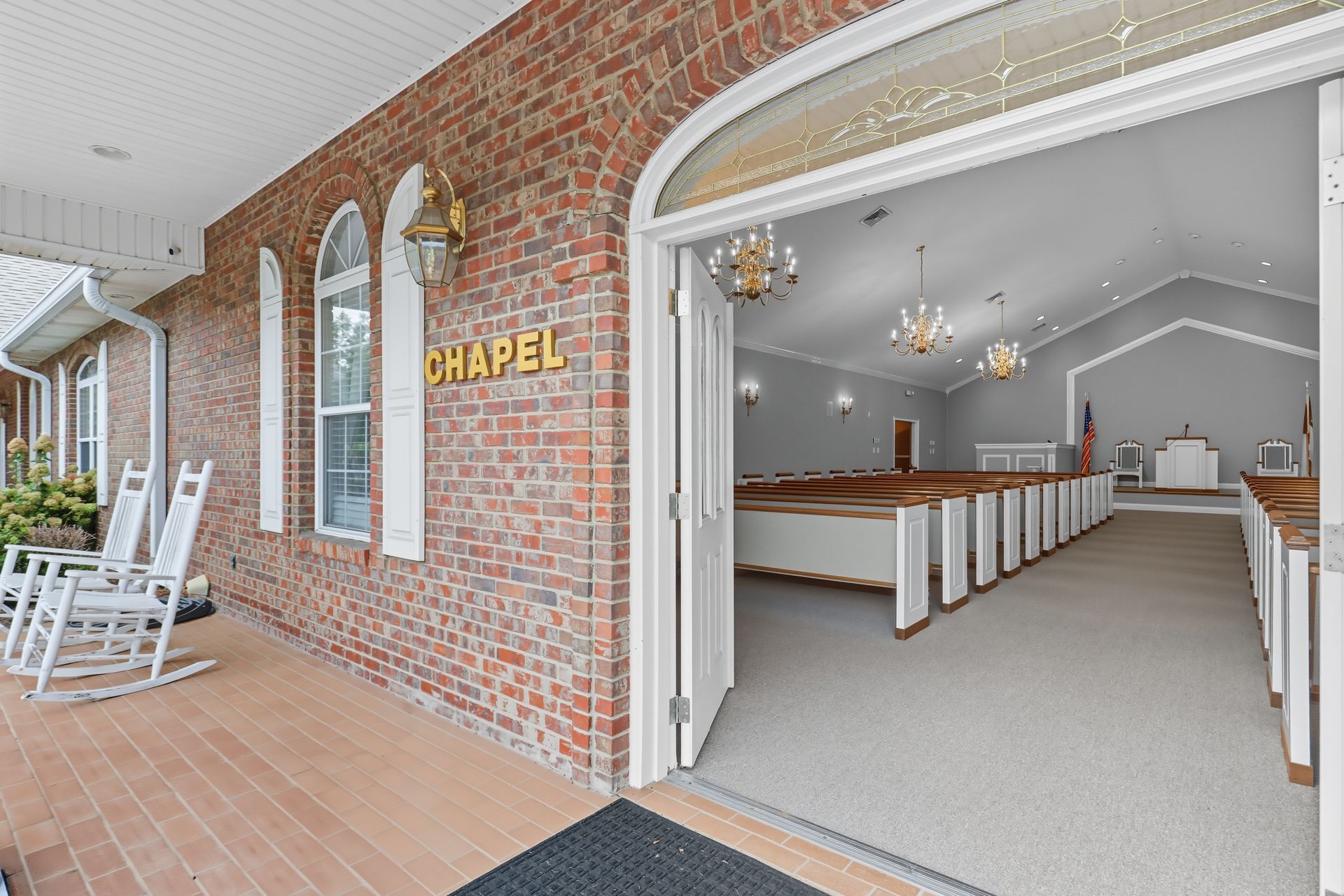 Open chapel entrance with brick exterior, white pews, and chandelier inside
