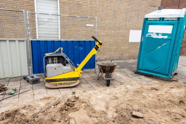 A yellow and black machine is sitting in the dirt next to a portable toilet.
