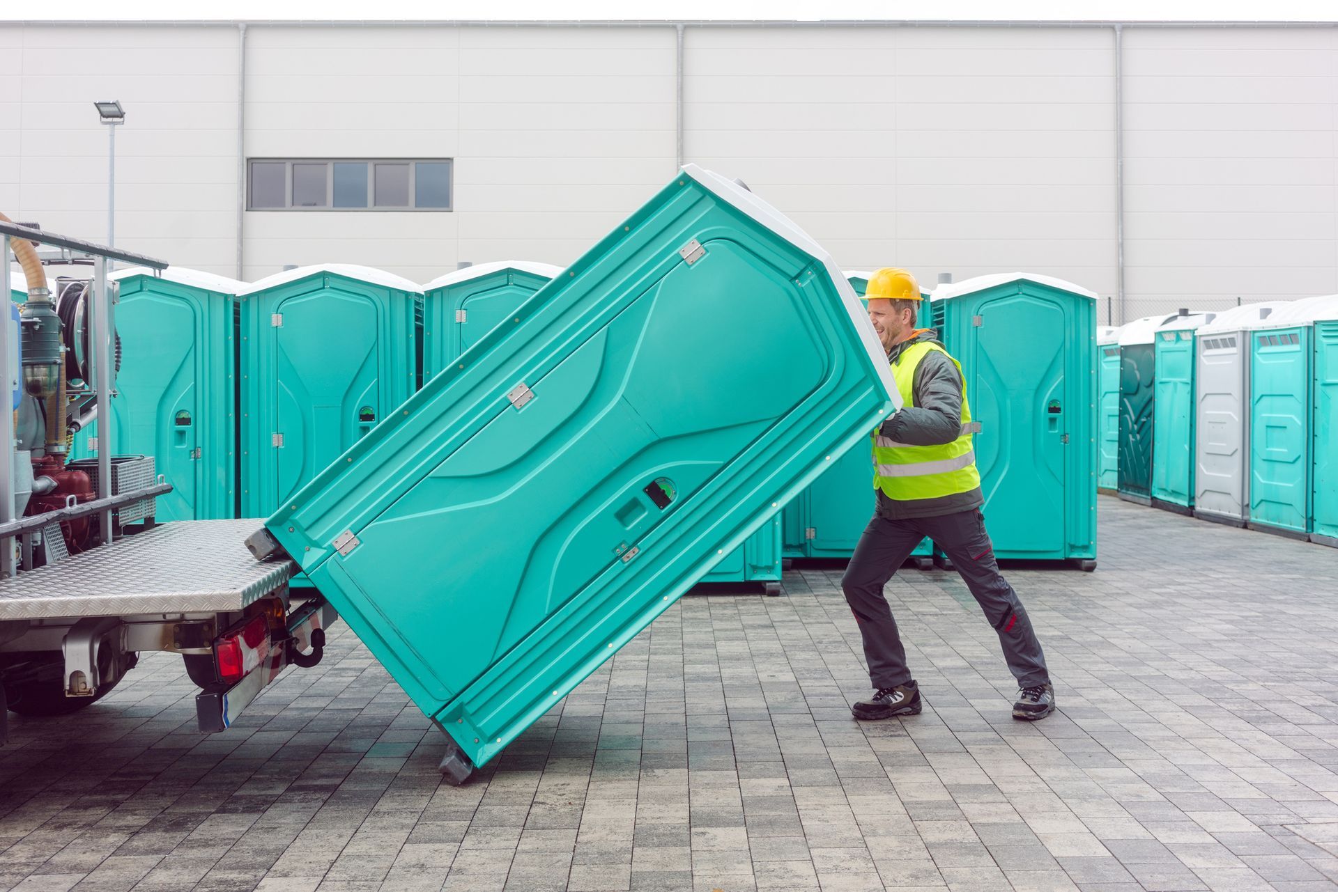 A man is lifting a portable toilet out of a truck.