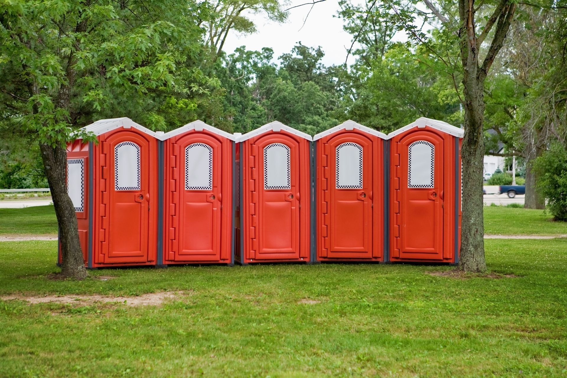 Five red portable toilets aligned outside, possibly in a park