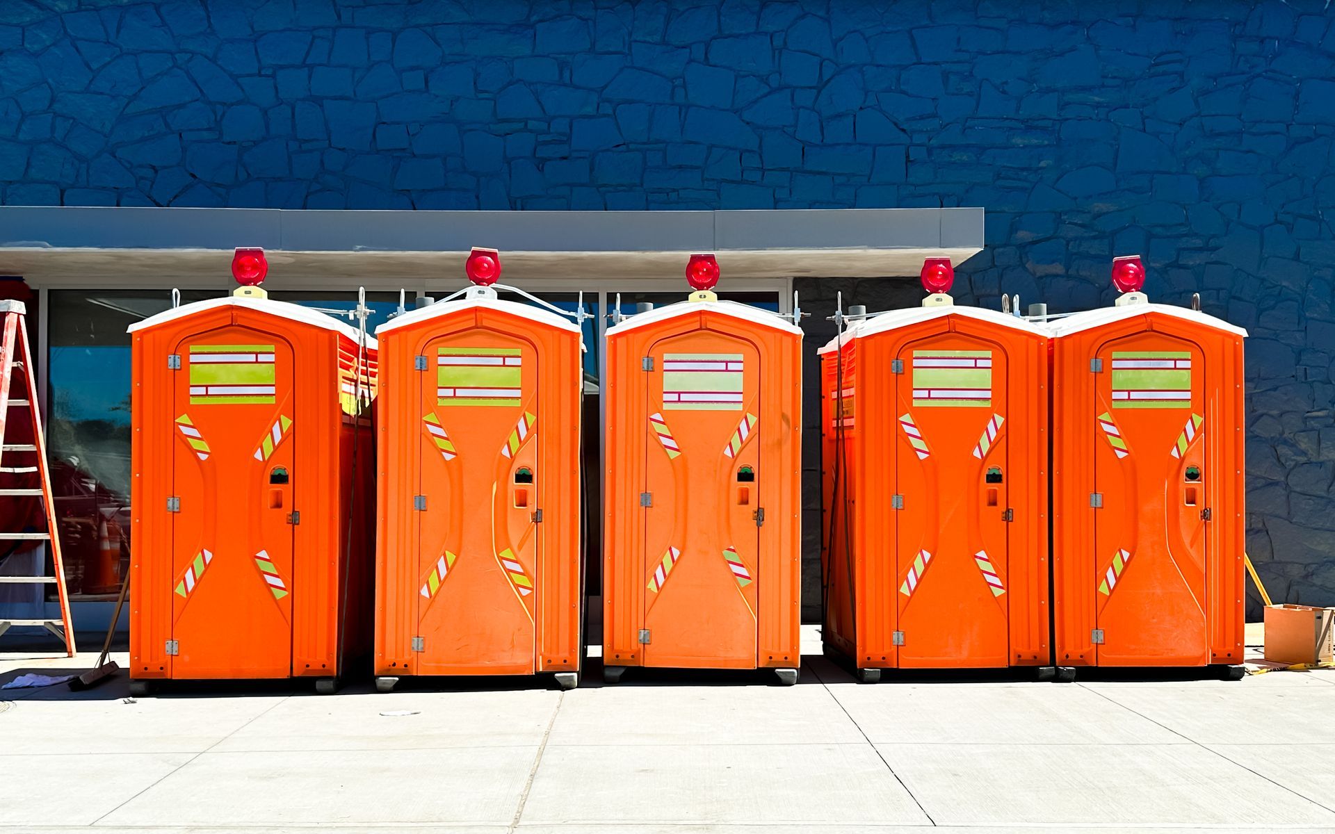 A row of bright orange portable toilets at a construction site.