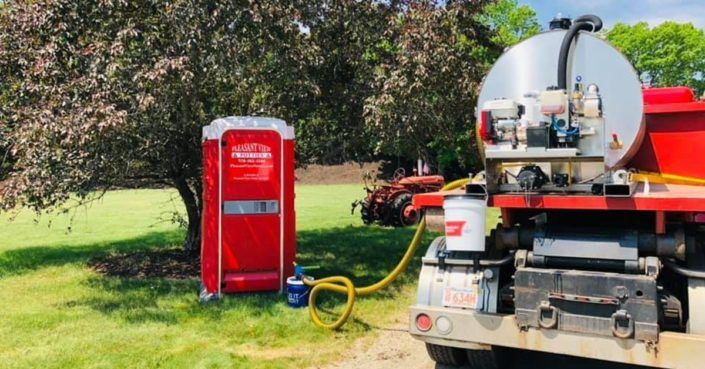 A red portable toilet is sitting next to a large truck.