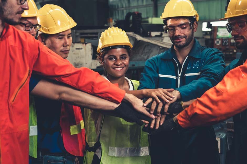 A group of construction workers are putting their hands together in a huddle.