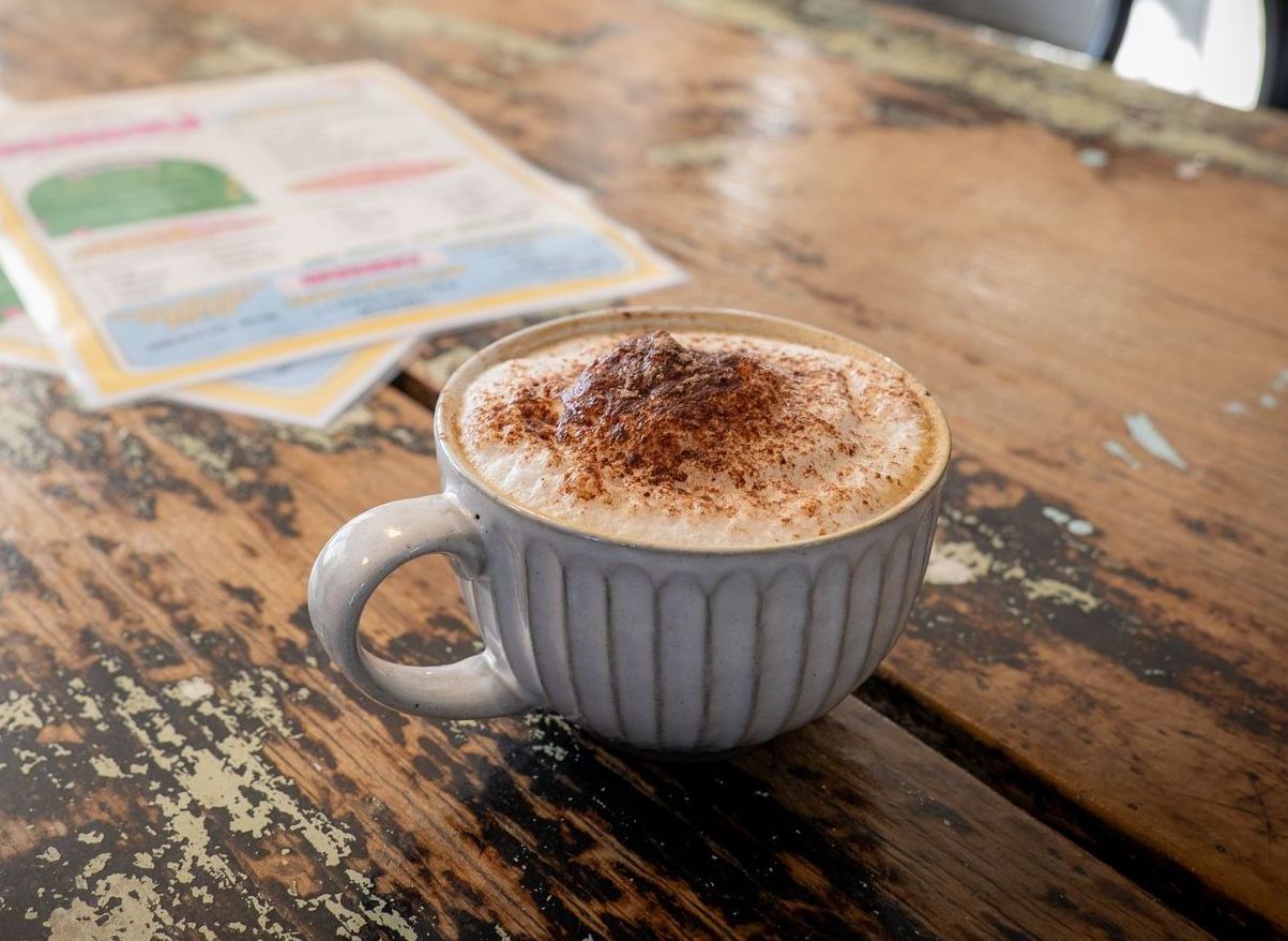 Cappuccino in a blue mug on a worn wooden table with a blurred document in the background.