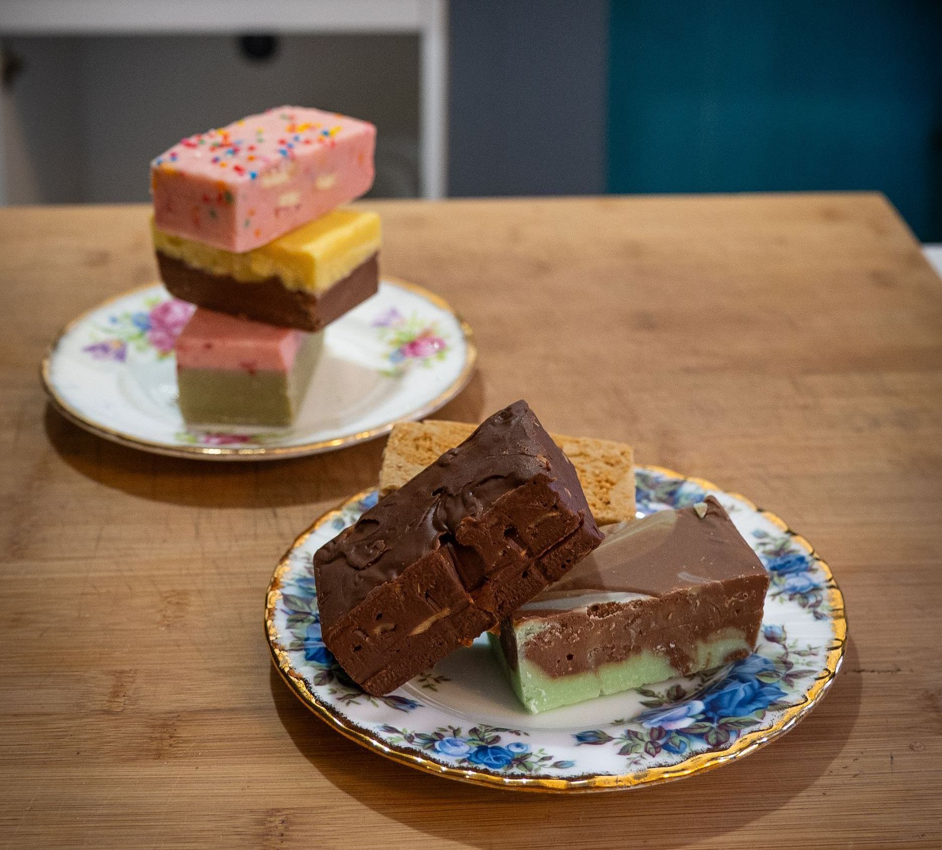 Fudge in various colors stacked on decorative plates on a wooden table.