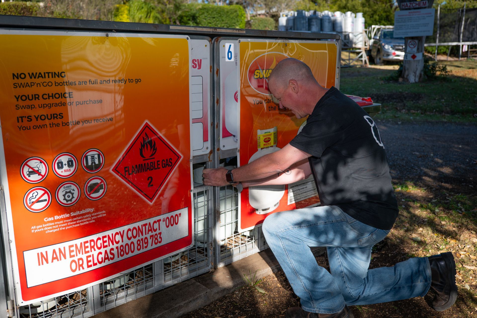 Man kneeling by a storage unit, opening a door. Unit has hazard warnings and text.