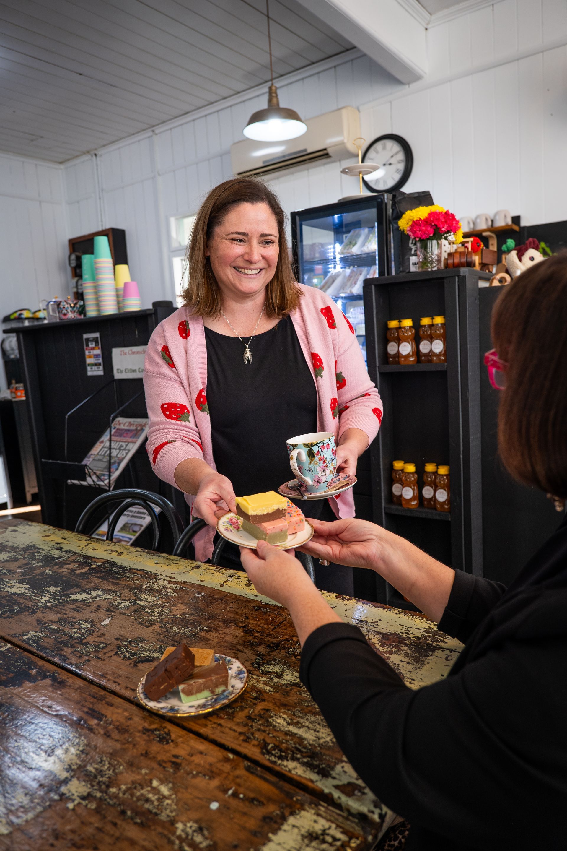 Woman serving tea and cake over a counter at a cafe.