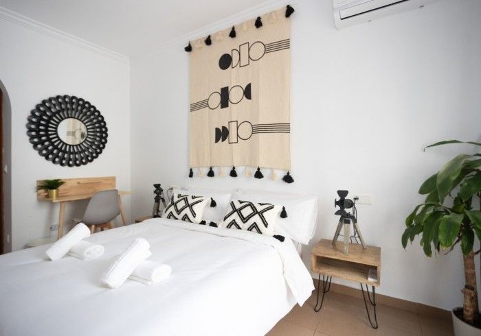 Un dormitorio con cama, mesita de noche, espejo y planta.
